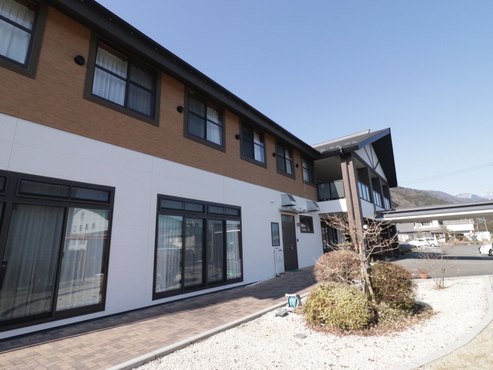 施設の建物は２階建てで、ホワイトとブラウンの外壁となっている。また広々とした敷地内には、ガーデンスペースを設置している。