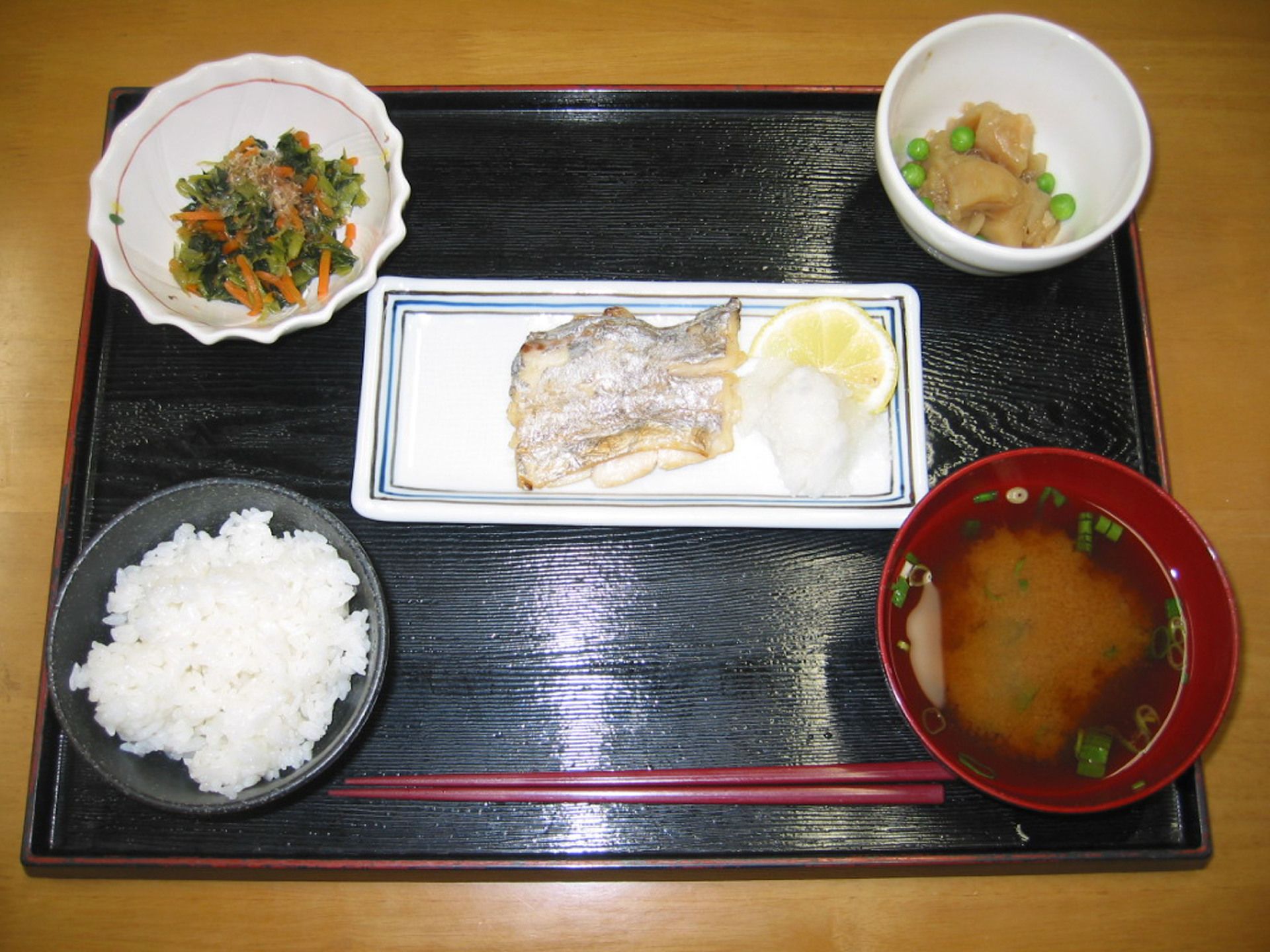 焼き魚、野菜の和え物や煮物などが黒いお盆に並べられている。魚と野菜を中心に立てられたバランスの良い献立になっている。