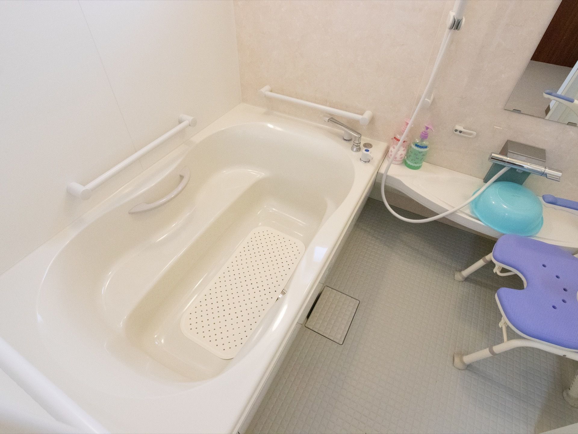 白を基調とした浴室で、浴槽内と壁に横型の手すりが設置されている。洗い場に青い洗面器が用意されている。