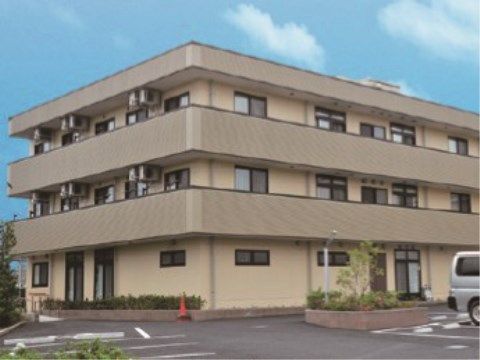手前に駐車場が広がっている、ベージュの３階建ての建物