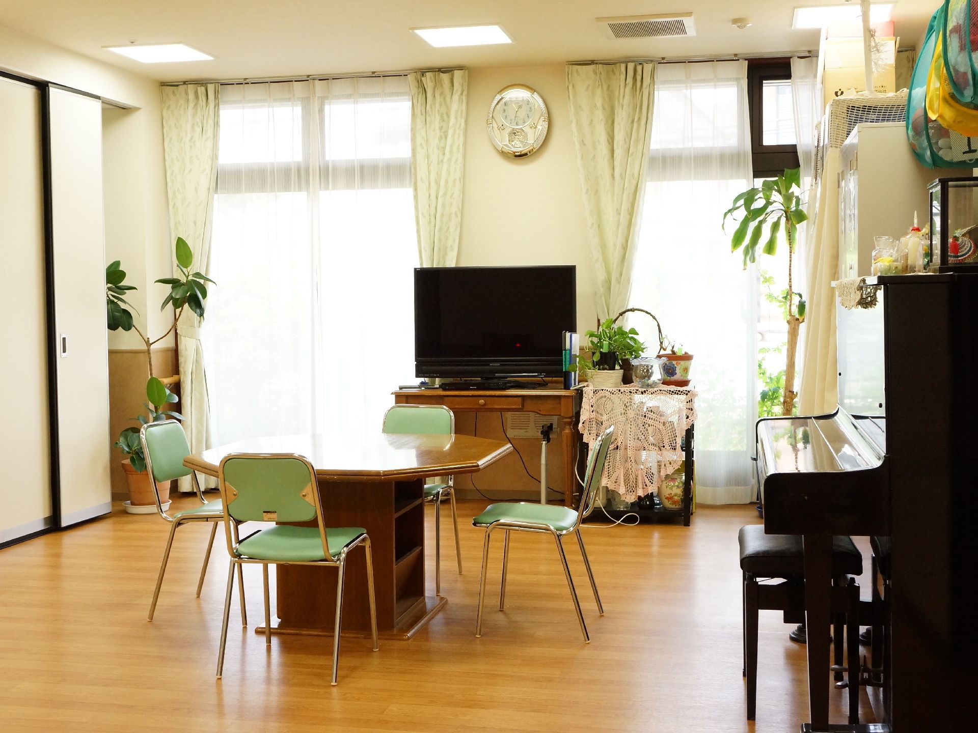 2つの窓からは明るい光が差し込んでいる。間の壁には時計がかかり手前にはテレビと室内にはテーブルや椅子も用意してある。
