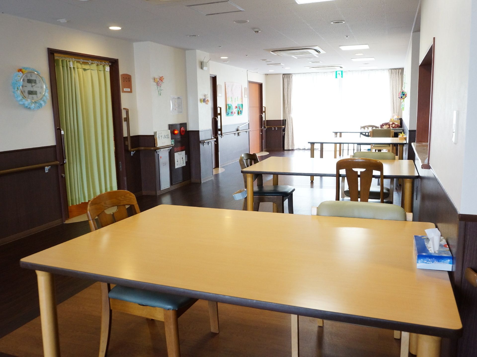 左手の壁には手すりが設置されており装飾品も飾られている。右手にはテーブルと椅子が何台も並んでおり突き当たりの窓から光が入り込んでいる。
