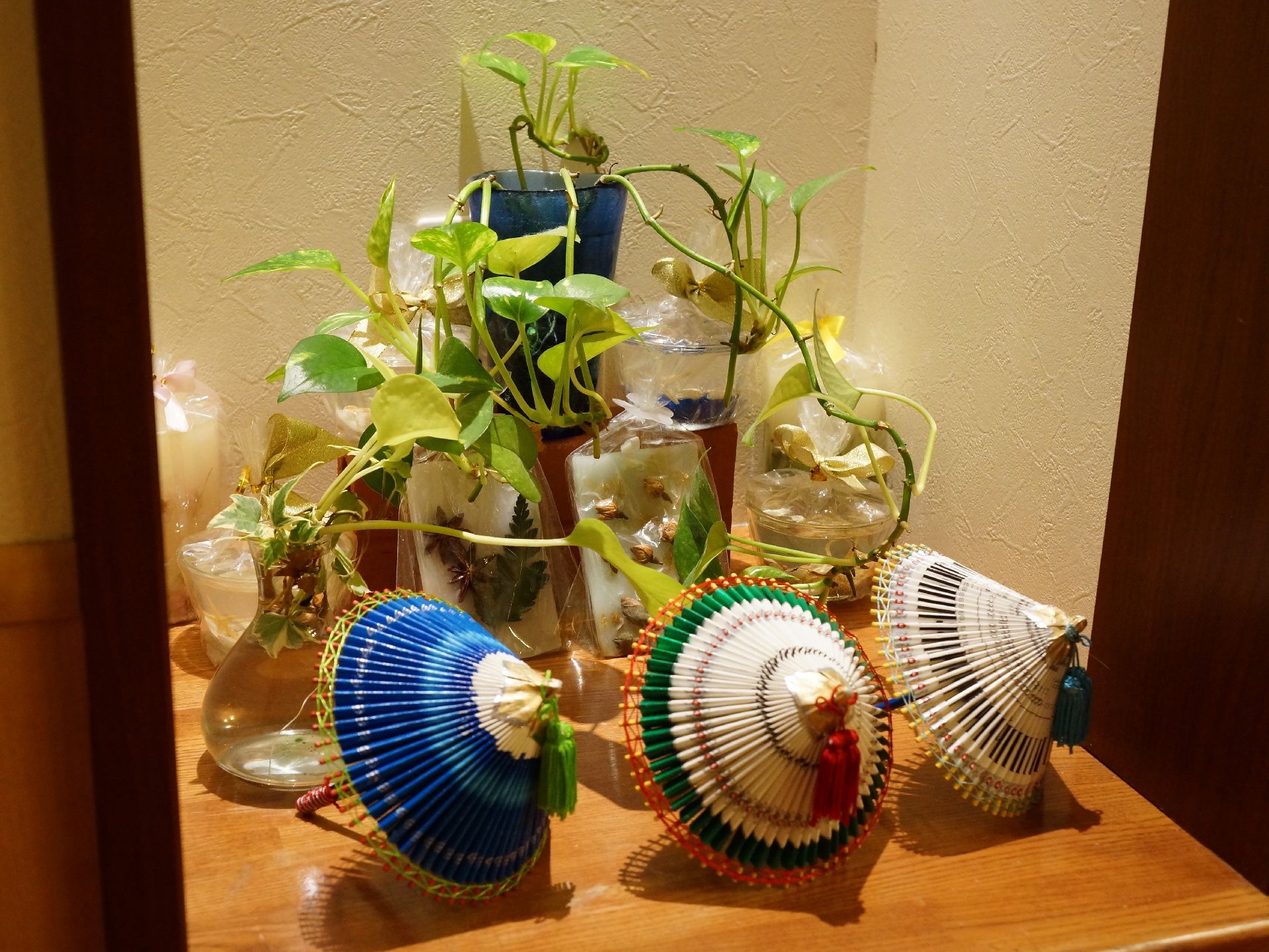 壁が凹んだところの木製の棚に様々な調度品が飾られている。観葉植物と3つの小さな傘がライトアップされている。