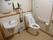 ベージュ系のストライプの壁が上品で清潔感のあるトイレには稼働式の手すりや円形の鏡と洗面台が設置されている。