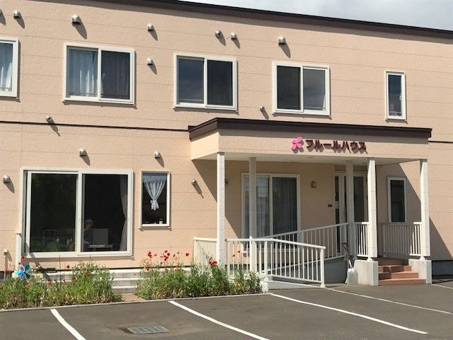 駐車場の手前の花壇に菖蒲の花が咲いている2階建ての施設前