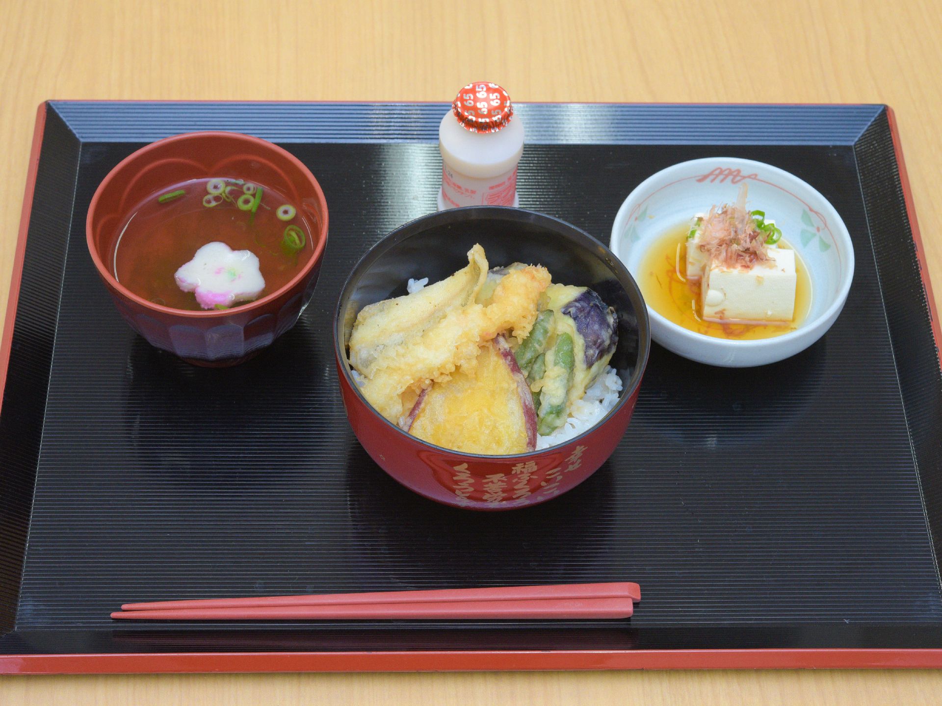 黒いトレーには、お吸い物や天丼、冷奴、乳酸菌飲料が並べられており、箸も置かれている。栄養のバラン考えて作られた食事である。