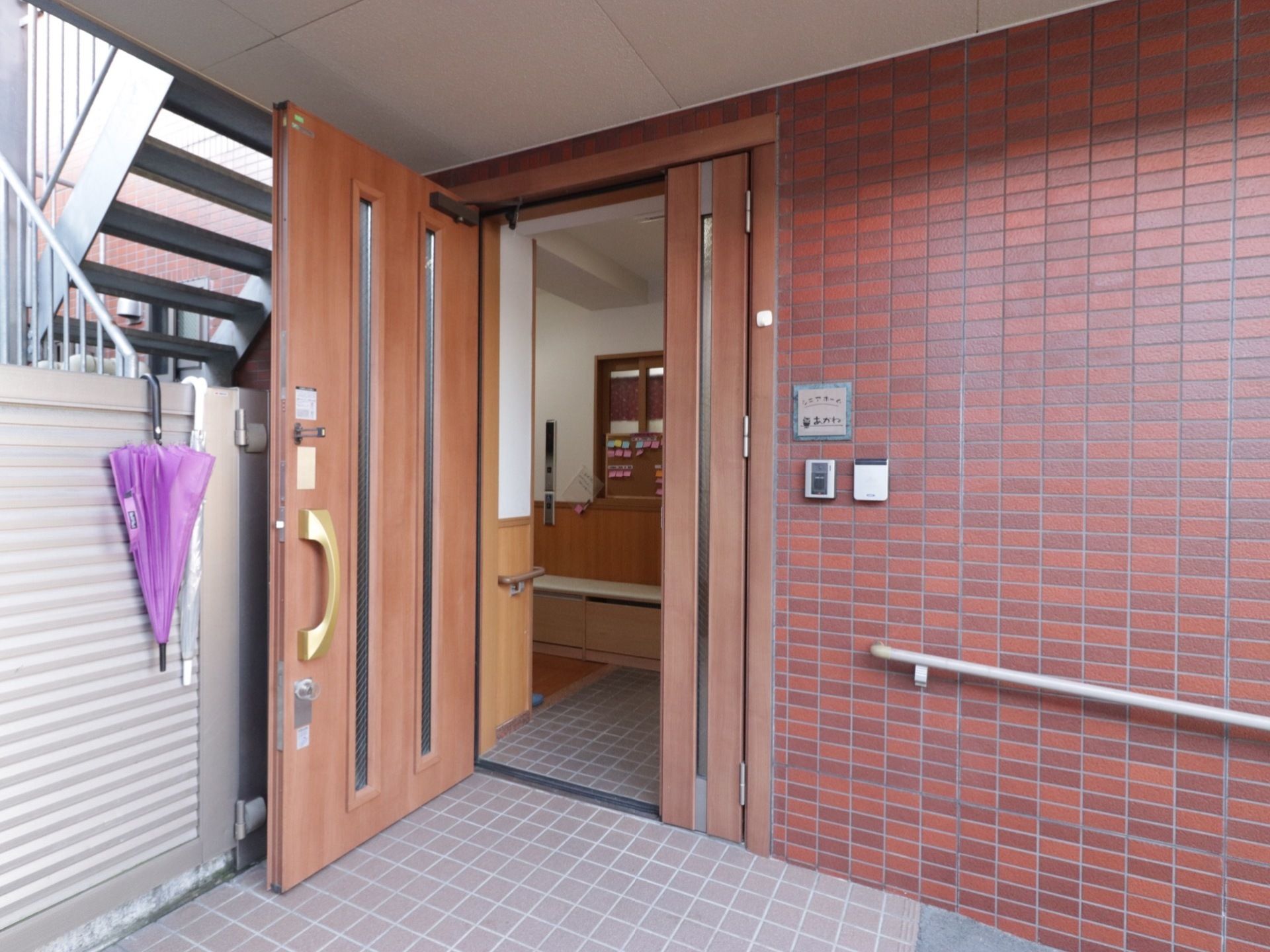 施設の玄関ドアは木製で、明り取りの窓を設けている。右側には施設名を書いたプレートとインターホンを設置している。