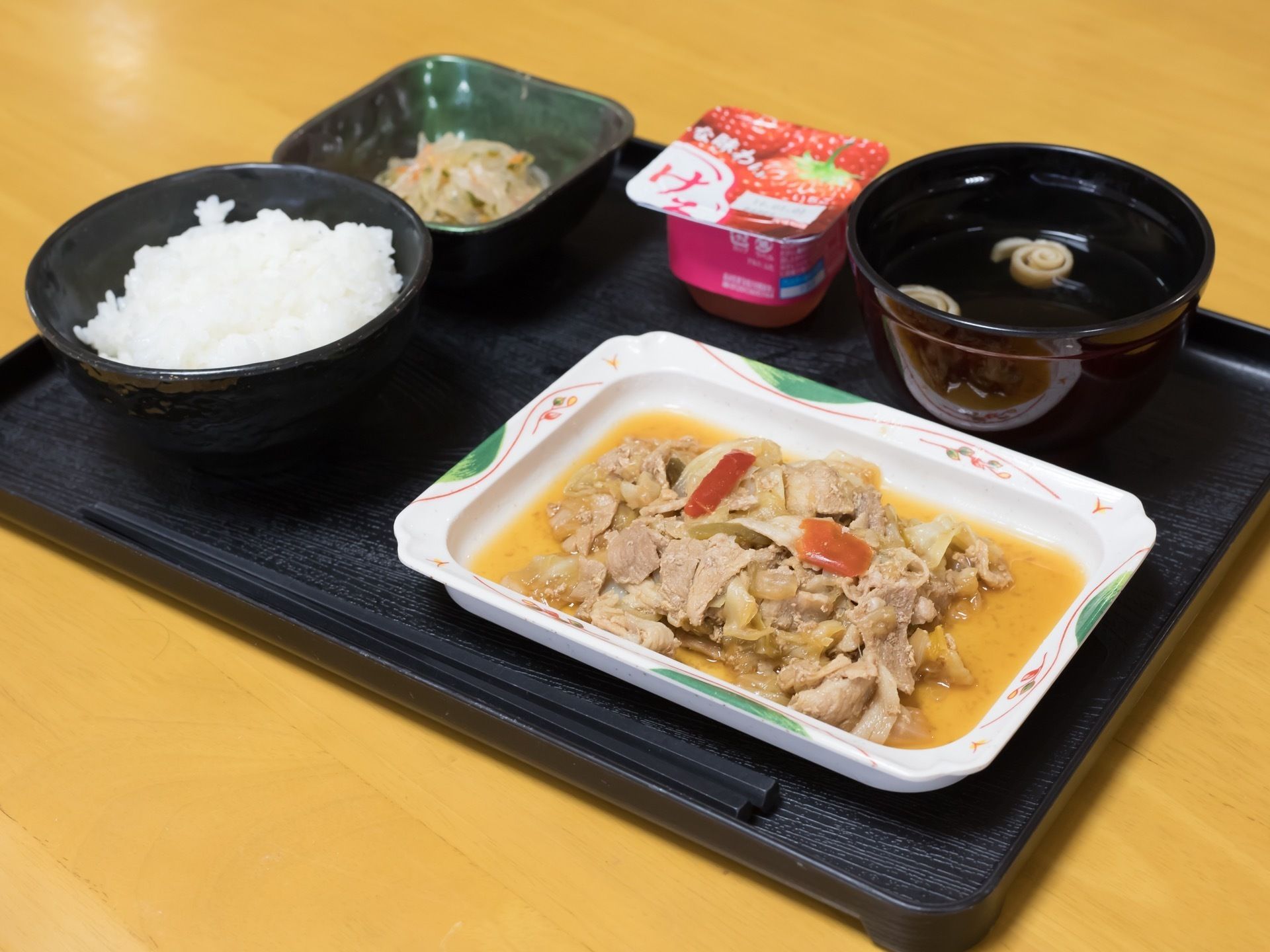 黒いお盆の上にお箸と食事が配膳されている。ご飯、お吸い物、メイン、副菜、デザートのメニューとなっている。