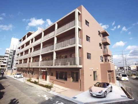 建物前に乗用車が２台停められている、ピンク色の建物
