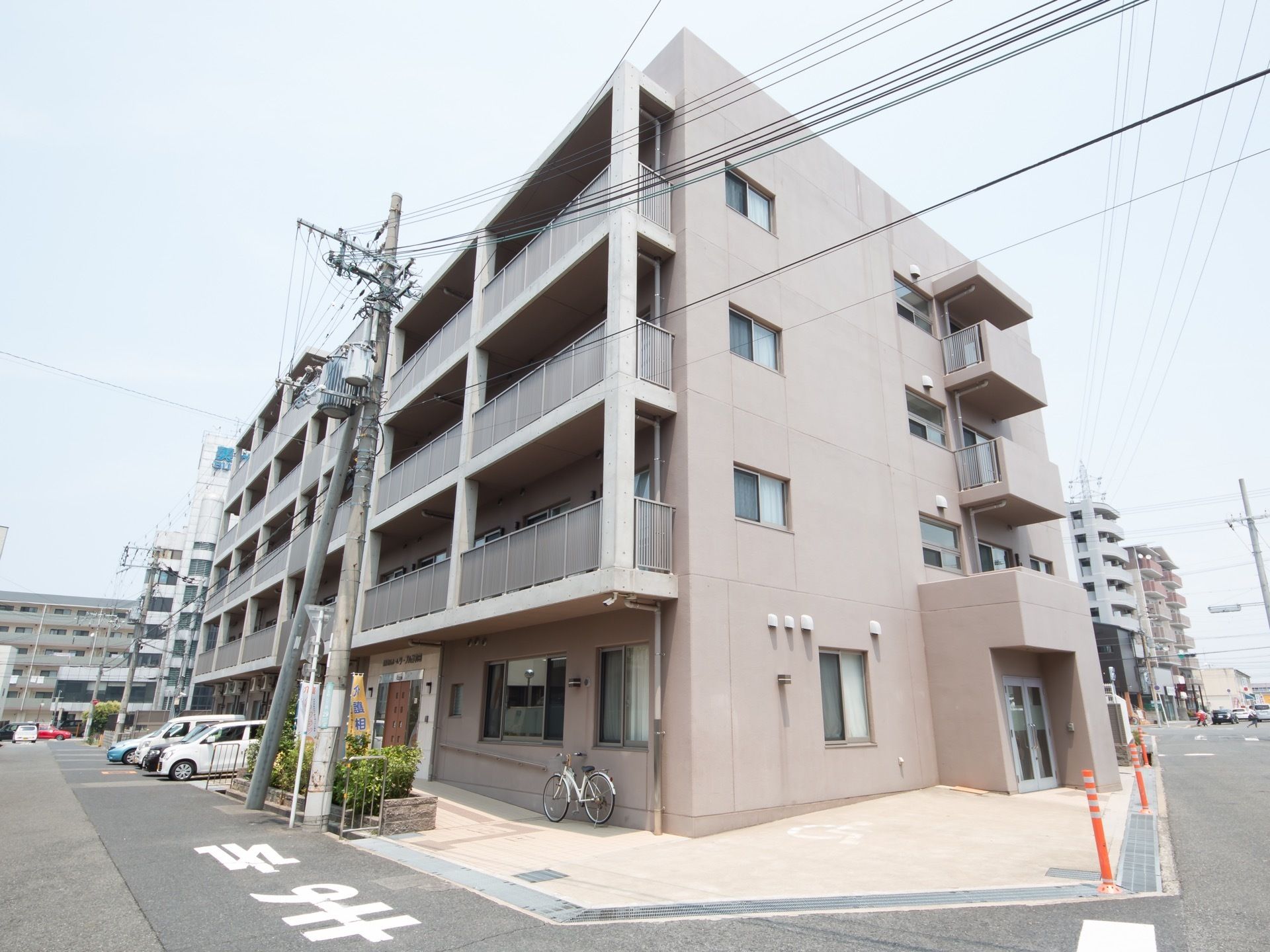 ４階建ての建物になっており、各部屋にバルコニーが設置されている。建物の下には駐車スペースがあり、車が数台停まっている。