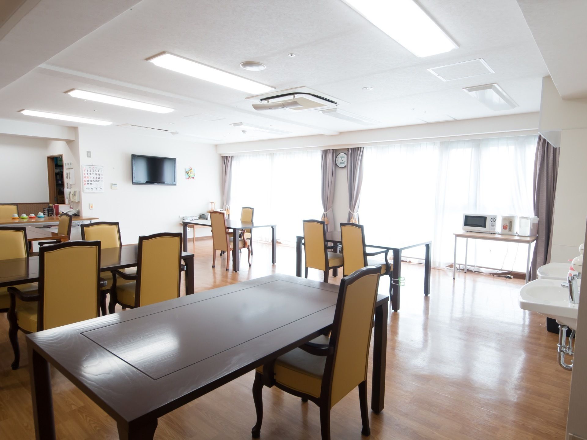 広々とした空間に、大きなテーブルと椅子があり、テレビや電子レンジが置かれている。手洗い場が設置されている。
