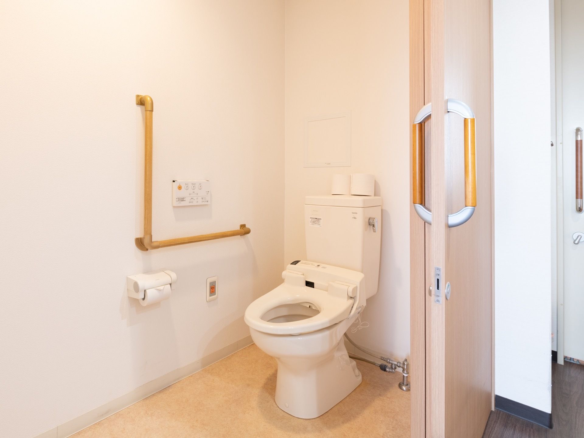 居室にあるトイレの入口は引き戸になっている。温水洗浄便座が設置されており、壁に操作パネルが取りつけられている。