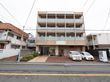 建物の前には道路が通っていて、敷地の一角には自動販売機が設置されている。道路から玄関へ向けて植え込みが作られている。