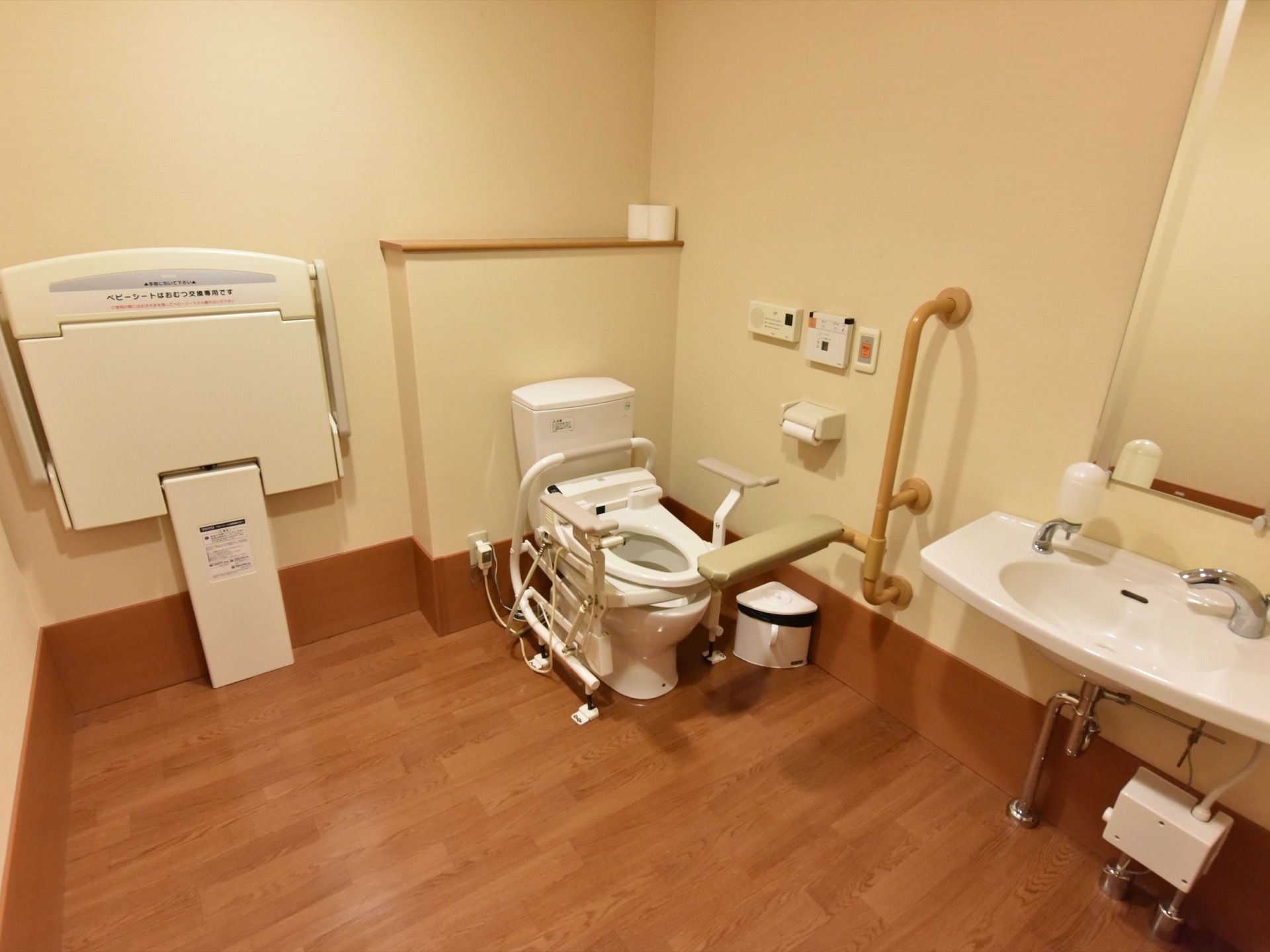 トイレはかなりスペースがあり、洋式便器だけでなくおむつの交換台や洗面台が取り付けられている。木目調が特徴的。