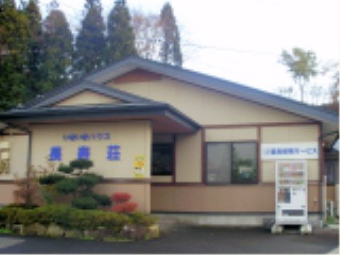 松の木やかえでの低木が生えた植え込みがある施設の入口