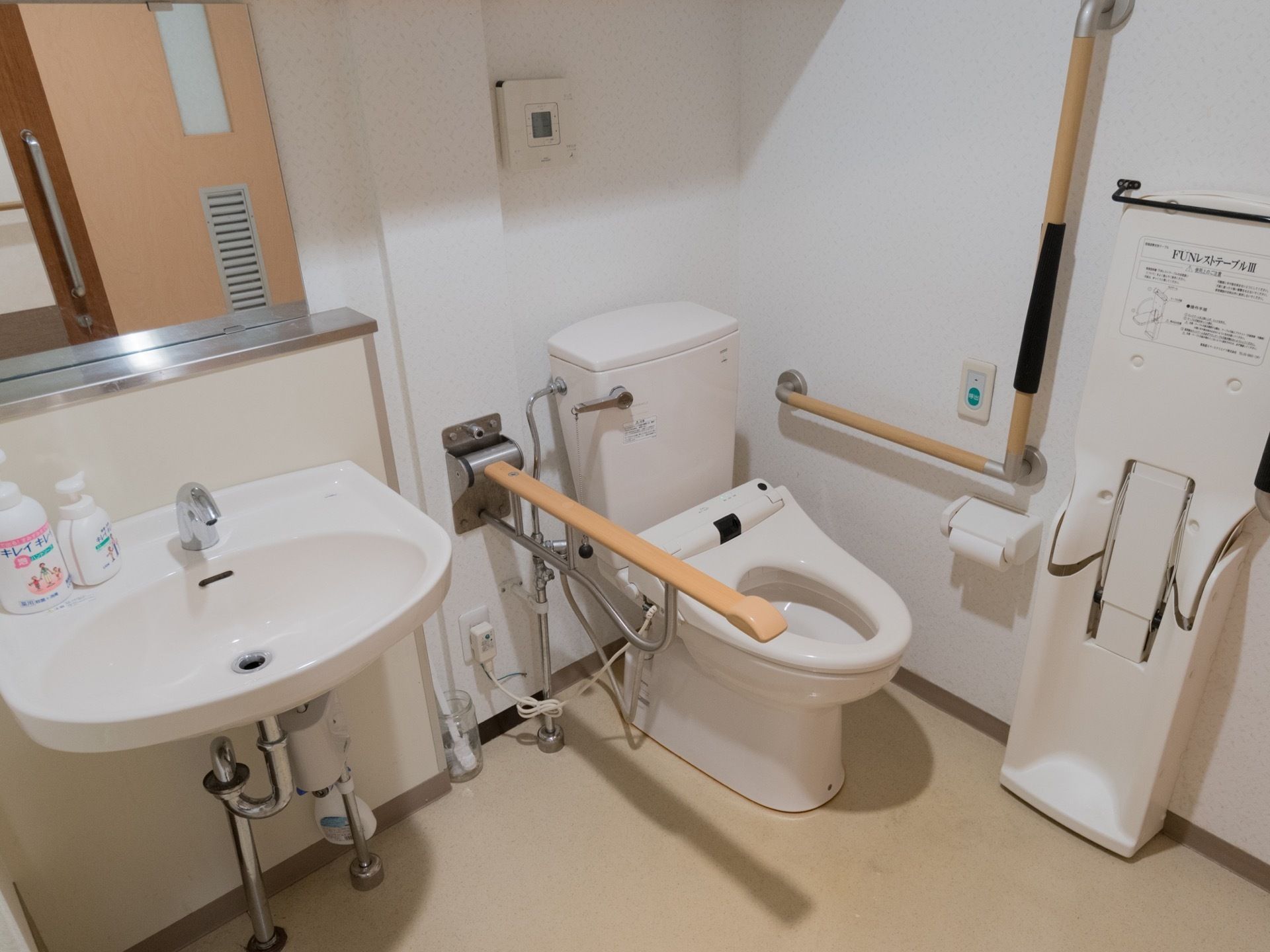 前傾姿勢を支えるためのテーブルや手すりが備わったトイレである。洗面台が側にあり、手を清潔に保ちやすい。