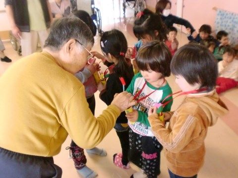 たくさんの幼児と手作りのペンダントを作って楽しむ入居者様
