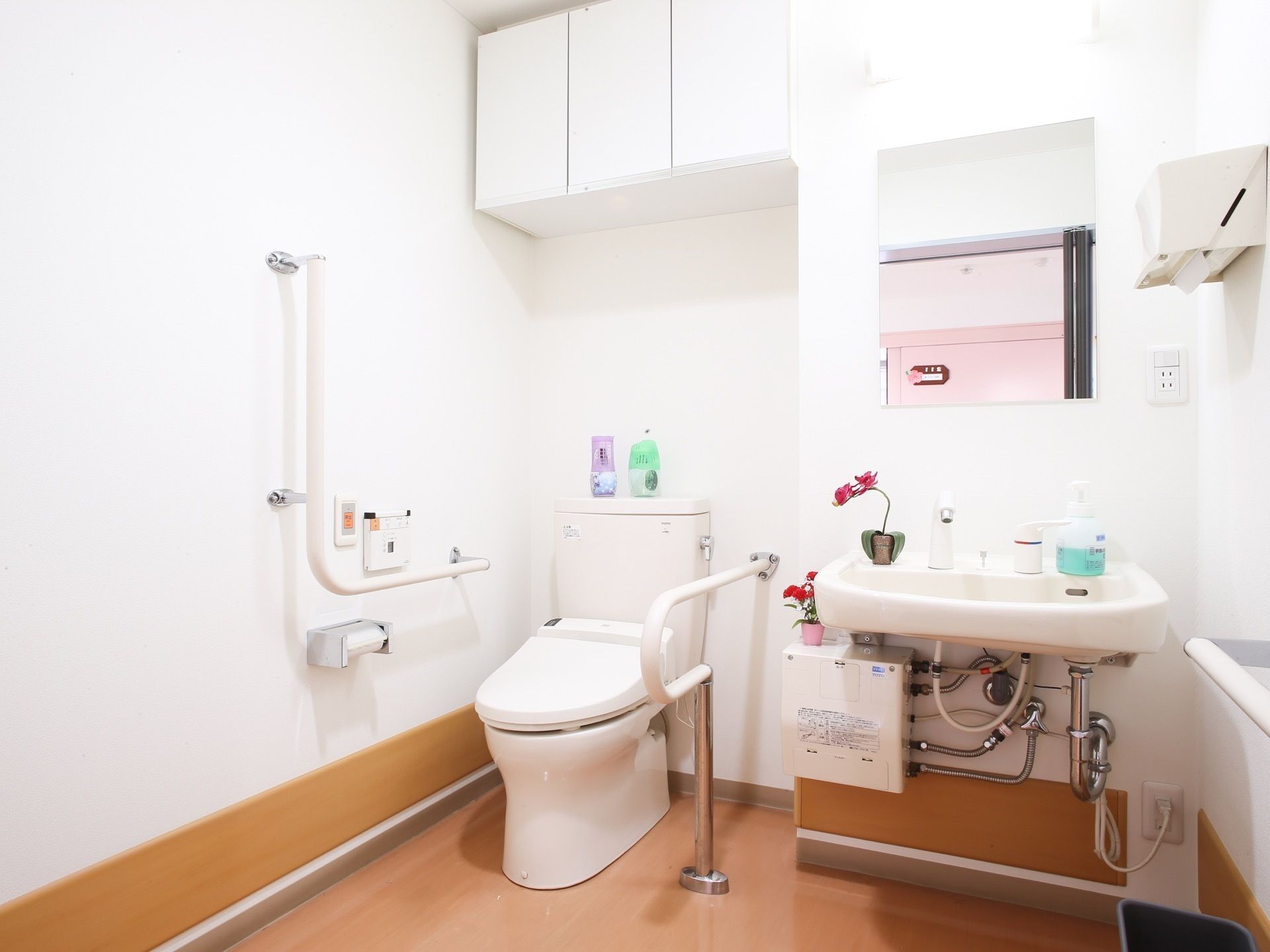 広々としたトイレの個室内に洋式の便器と洗面台が設けられている。手すりや緊急時呼び出しベルが備わっている。