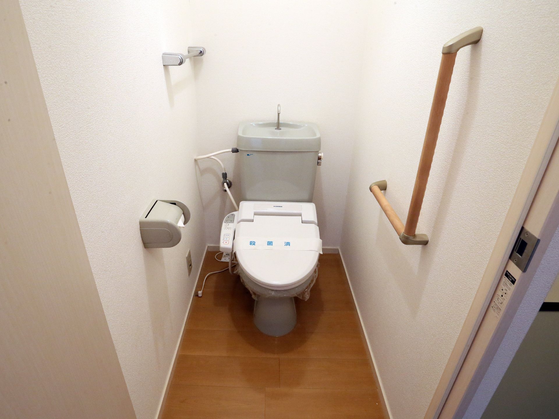 トイレはバリアフリーで温水洗浄機能付きである。壁には動作を助けるL字型の手すりやタオル掛けが設置されている。