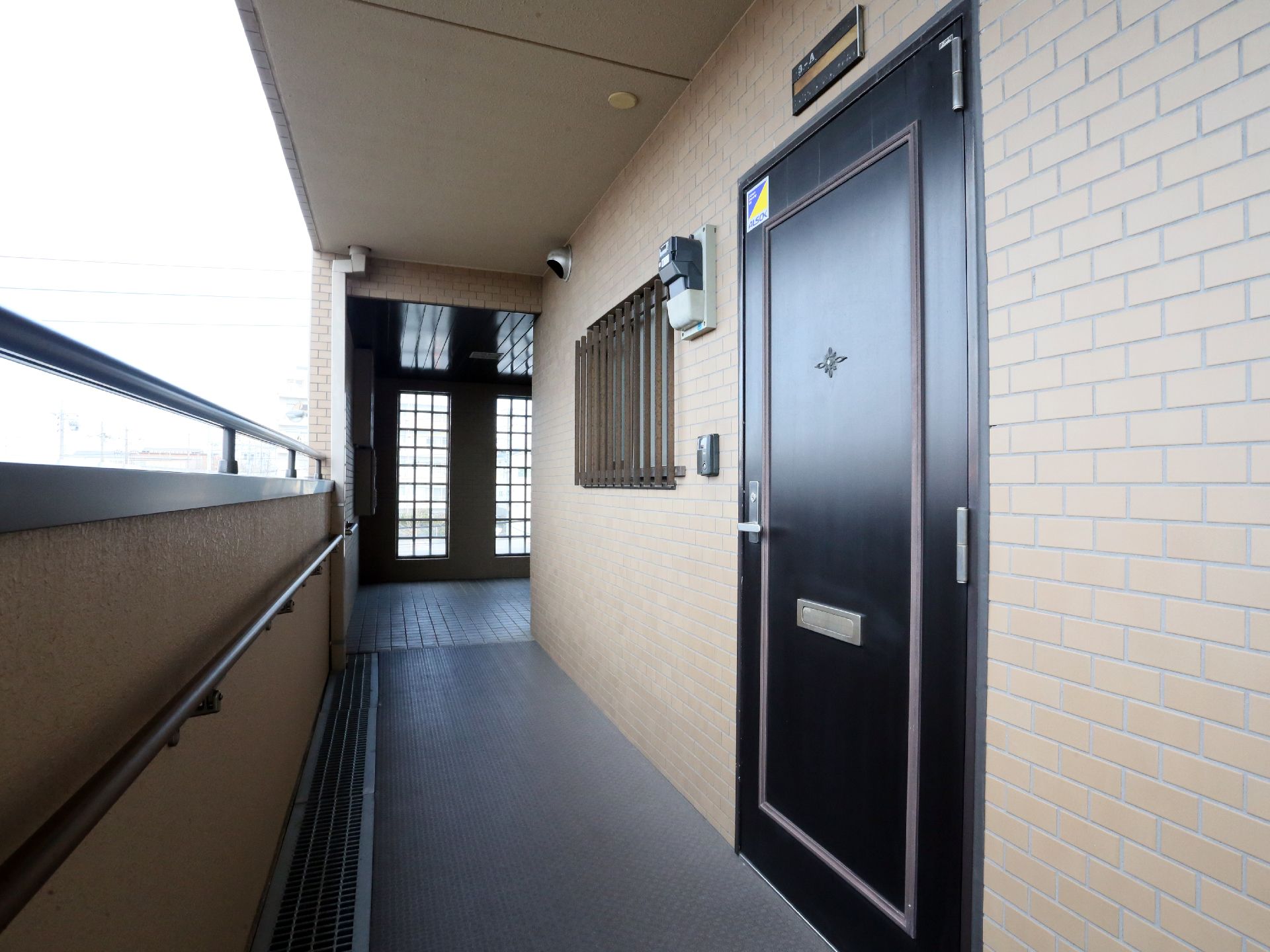 外廊下の壁には安全面を考えて上部と中間部に手すりが取り付けられている。真っ直ぐな廊下の先には広いエレベーターホールがある。