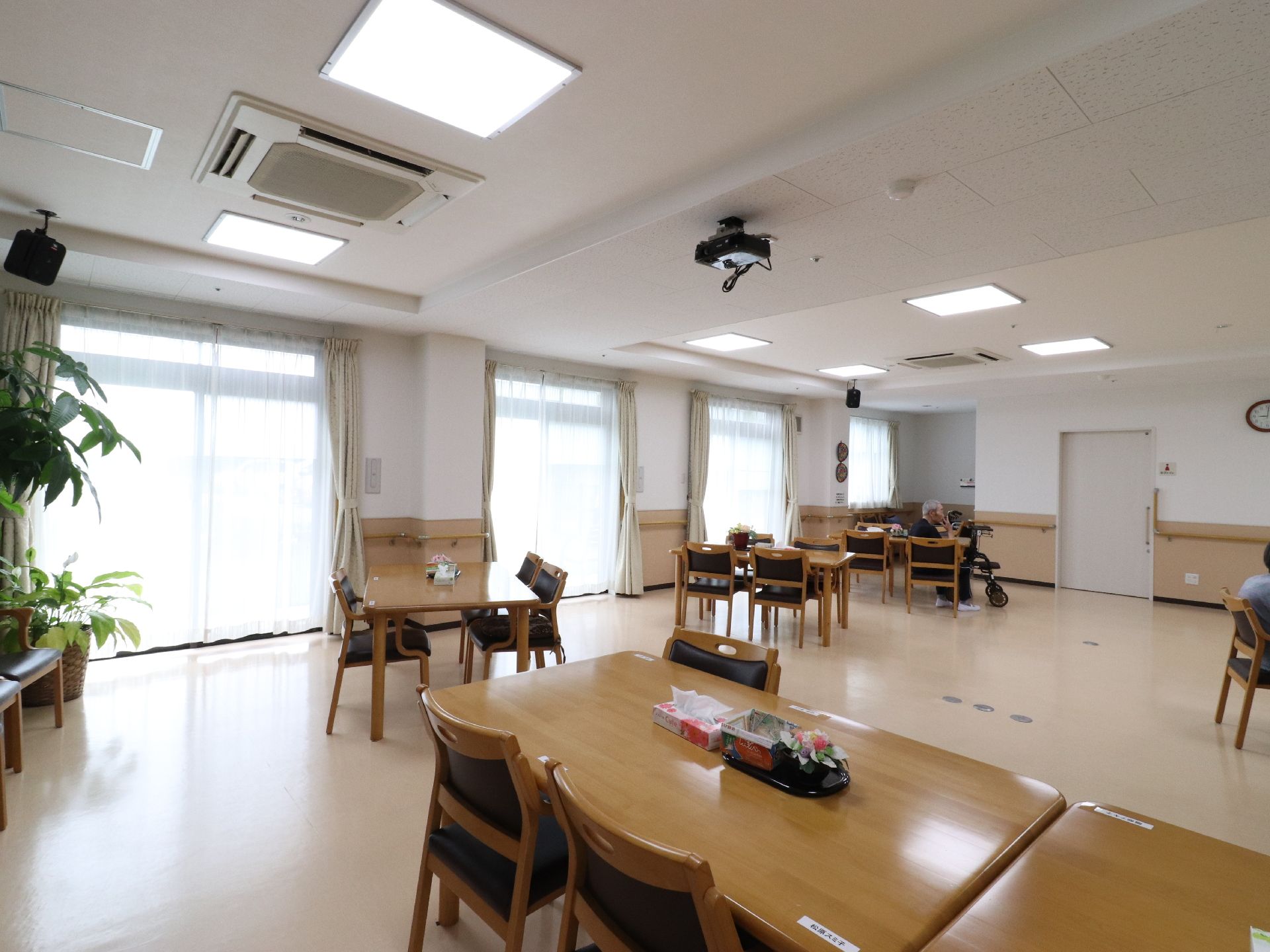 日の光がよく入る、広々した空間である。大きめのテーブルといすが設置されている。テレビがあったり、手すりも設置されている。