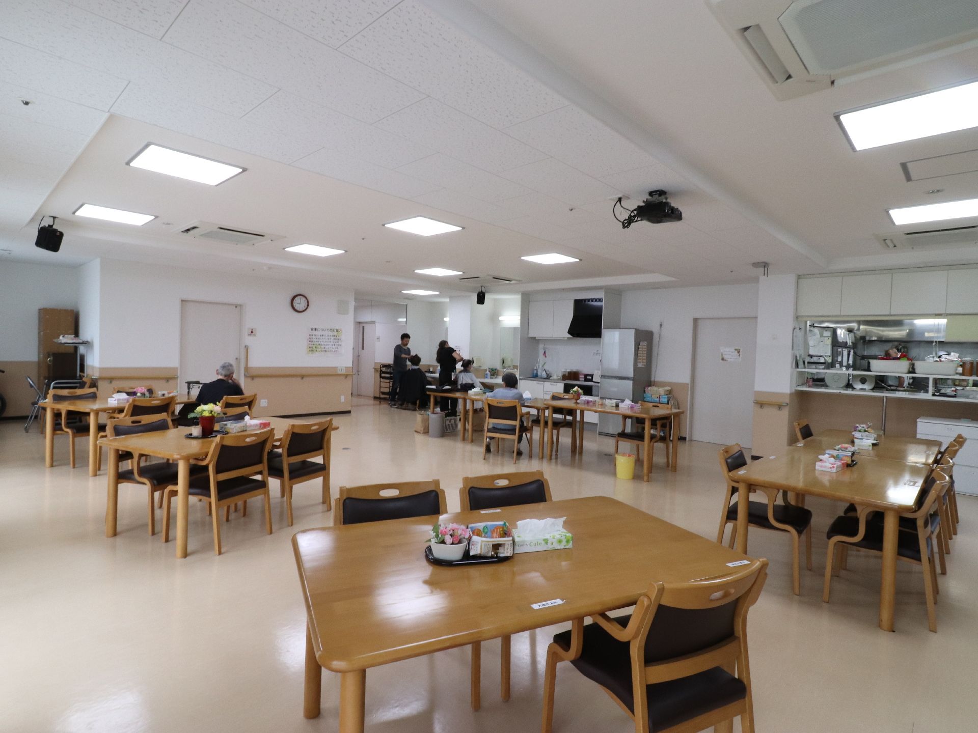 食堂は車いす利用者の方も同じテーブルで食事を摂れるよう、充分なスペースが確保されている。天井には、スピーカーや空調がある。