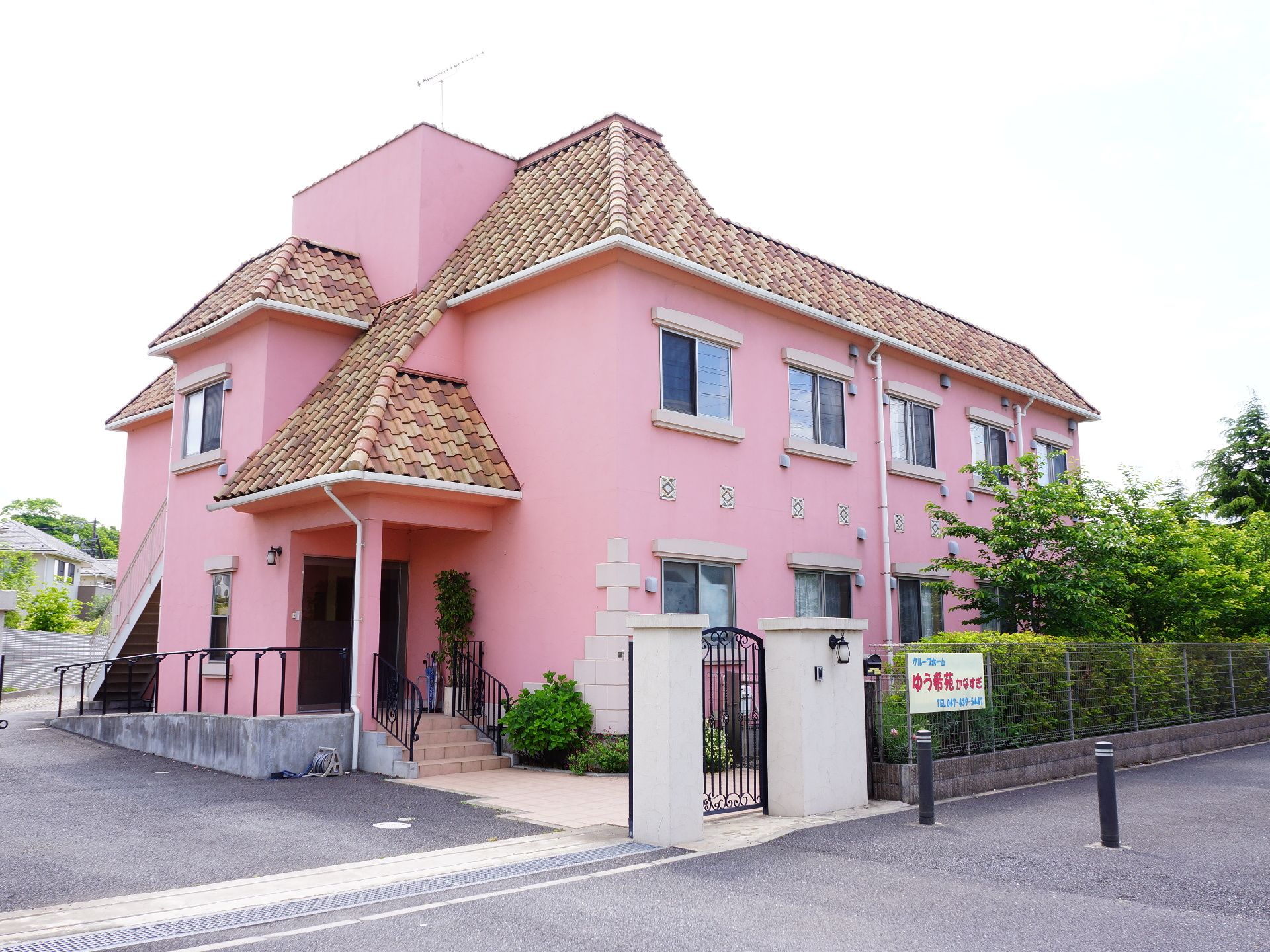 ピンクの外壁が印象的な施設の建物。色違いの瓦が南欧風でアクセントにもなっている。外観の可愛らしさから利用者にも馴染まれている、