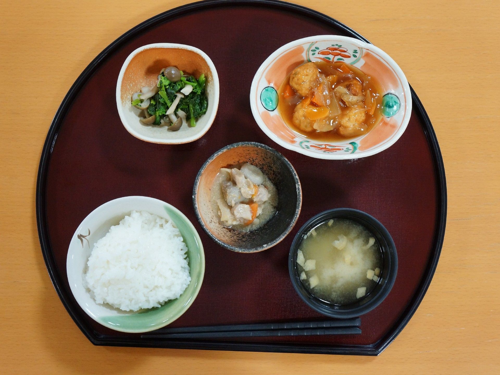 茶色のお盆に乗った酢豚定食。品数は多いが一品ずつは少量である。