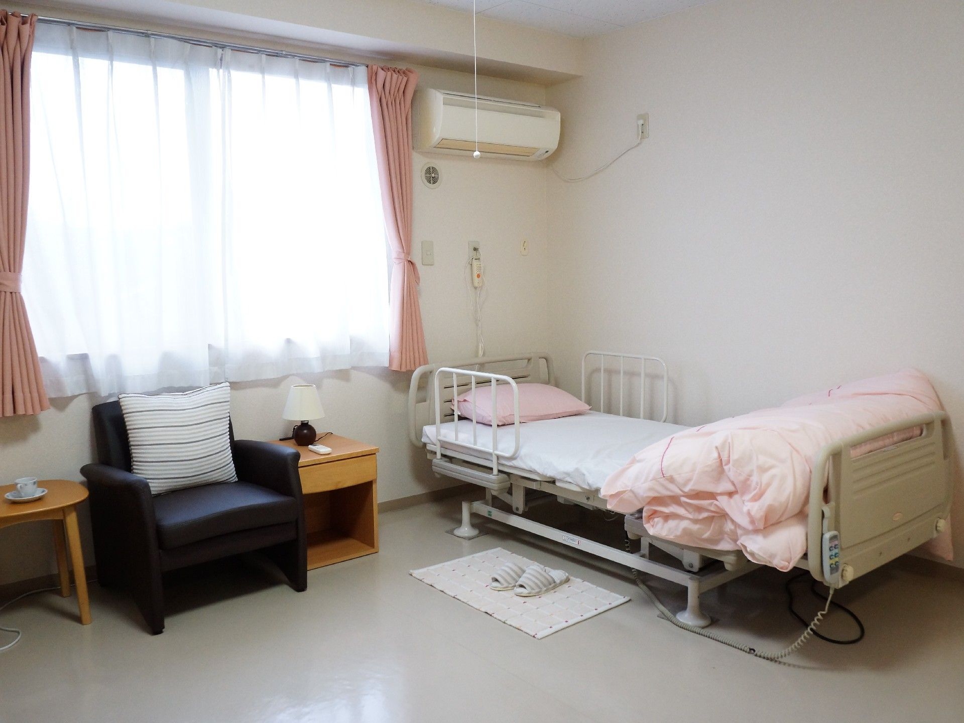 寝具カバーやカーテンをピンクで統一してた居室。テレビやソファーチェアが備え付けられている。