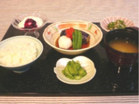 黒くて四角いおぼんに並べられた煮物やおひたしなどの食事