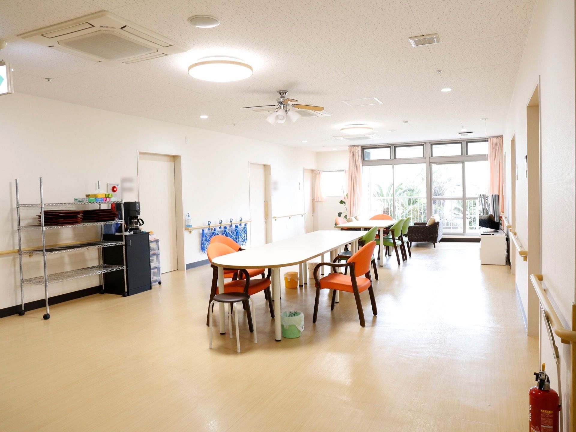 部屋の中央にダイニングテーブルと椅子が並べられ、壁際にはスチールラックとコーヒーメーカーと消火器が置かれている。