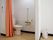 タンク付き洋式トイレが設置されている。壁には手すりと２連のペーパーホルダーと非常ボタンが取り付けられ、カーテンが掛けられている。