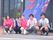 性別や年齢の違うスタッフが暖簾の前に並んで座っている。左横には、花のプランタが置かれており、外水道が後ろの壁際に設置されている。