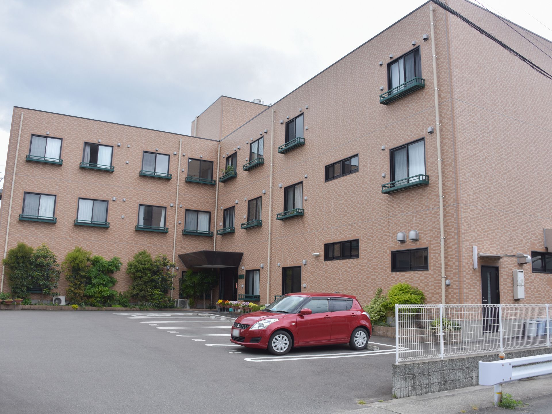 外観は、3階建てのタイル貼りの建物である。植栽も綺麗に植えられている。駐車スペースが広くとってある。