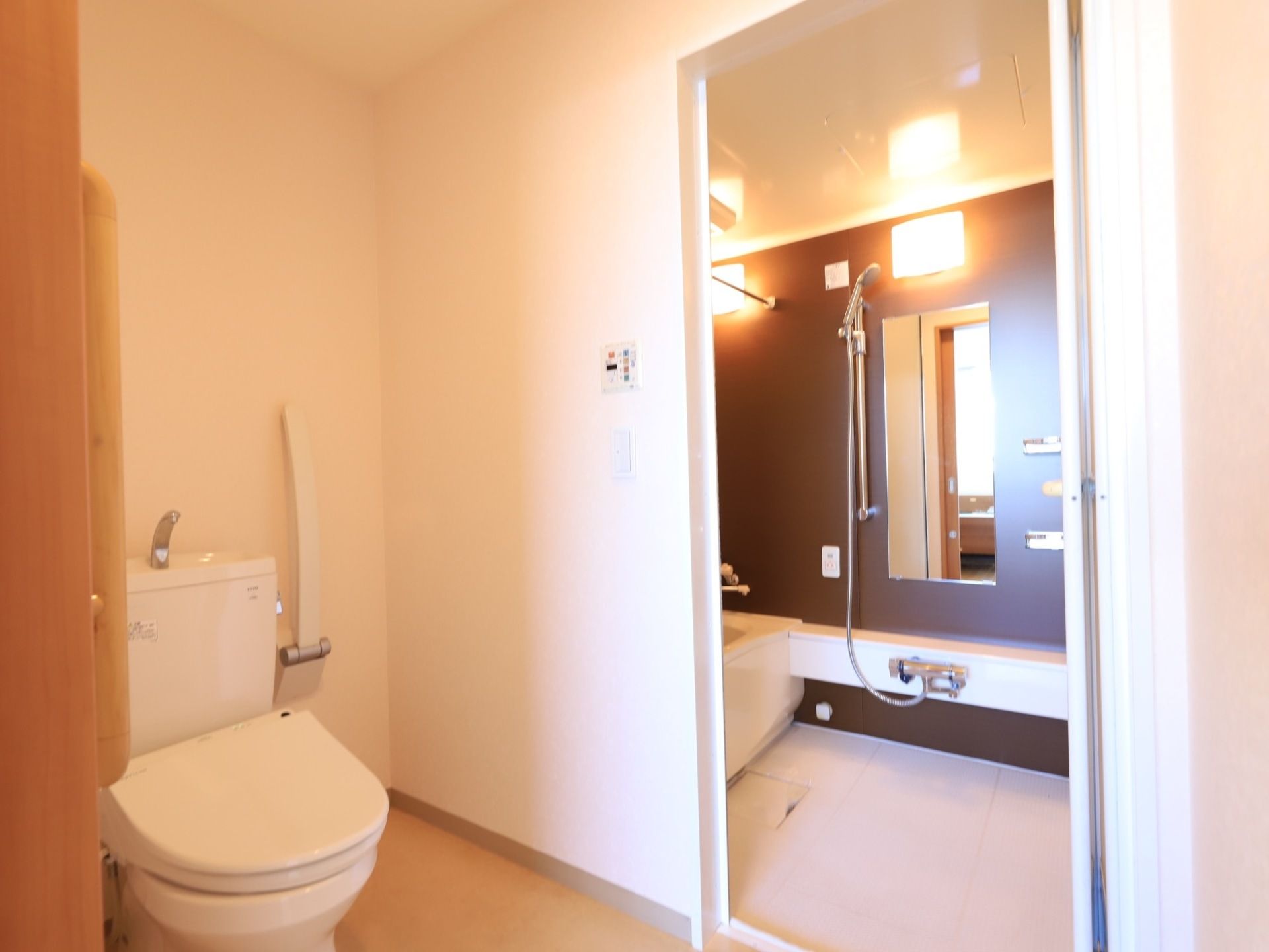 居室のトイレは白で統一された空間で清潔感がある。折りたたみ式の手すりが備わっている。隣は浴室で導線を考えた配置になっている。