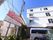 施設の名前が書かれた大きな看板が立てられている。建物の近くに車やバイクが駐車できるようになっている。