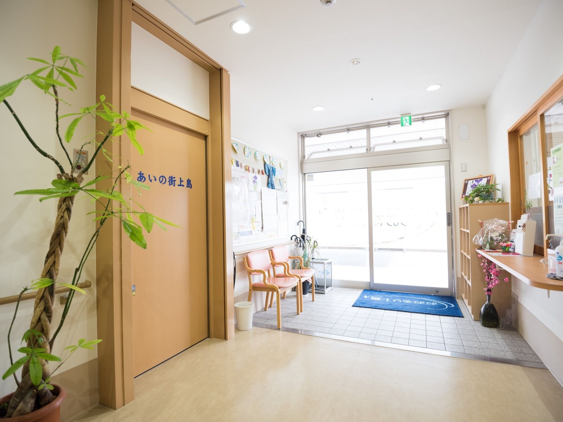 ガラス張りの自動ドアのある玄関。横には受付窓口がある。足元には段差がなく、玄関マットが敷かれ、側には椅子が並べられている。