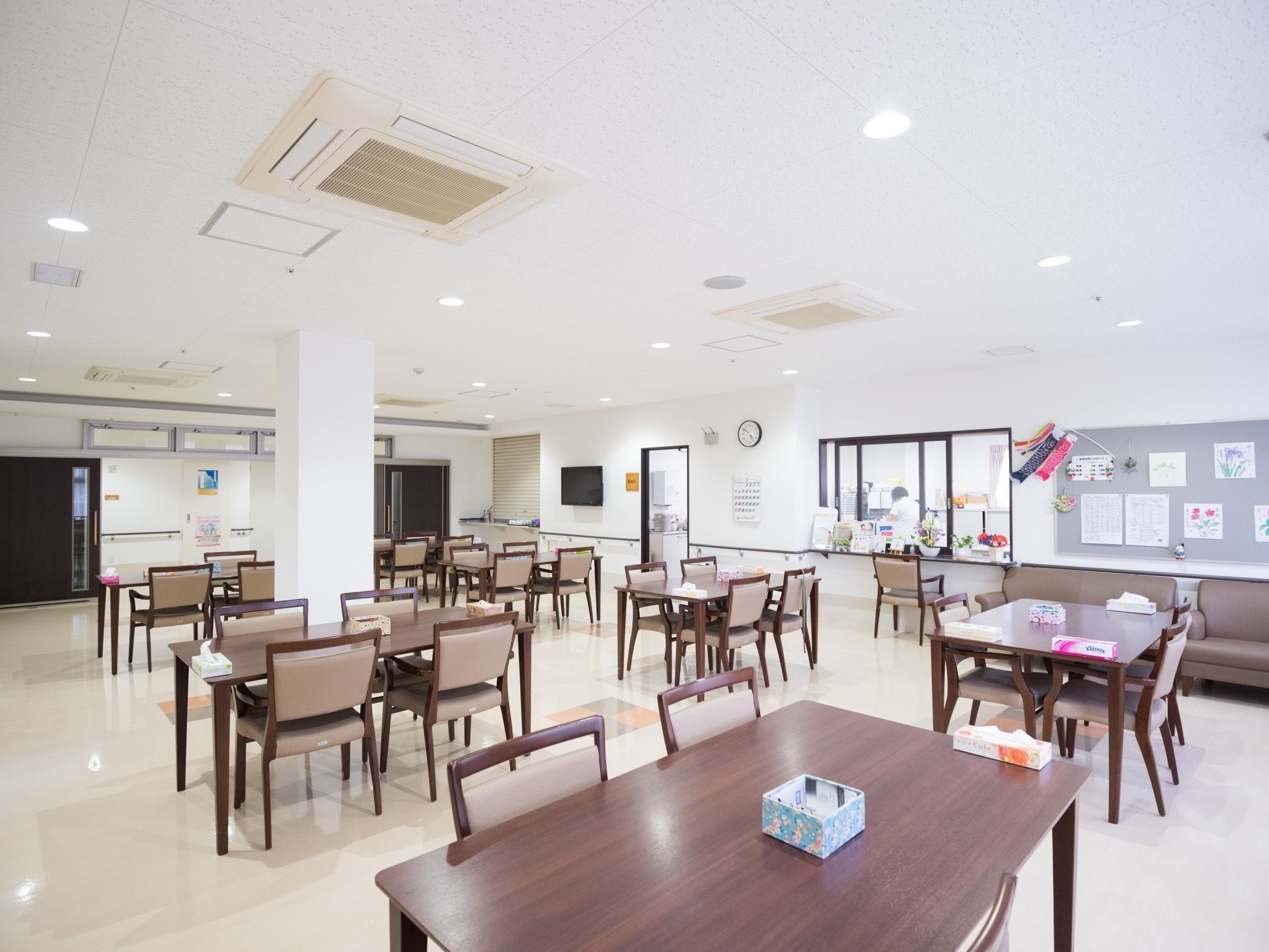 広々とした食堂がある。複数のテーブルの周りにはそれぞれ椅子が並べられている。壁際にはソファーがある。
