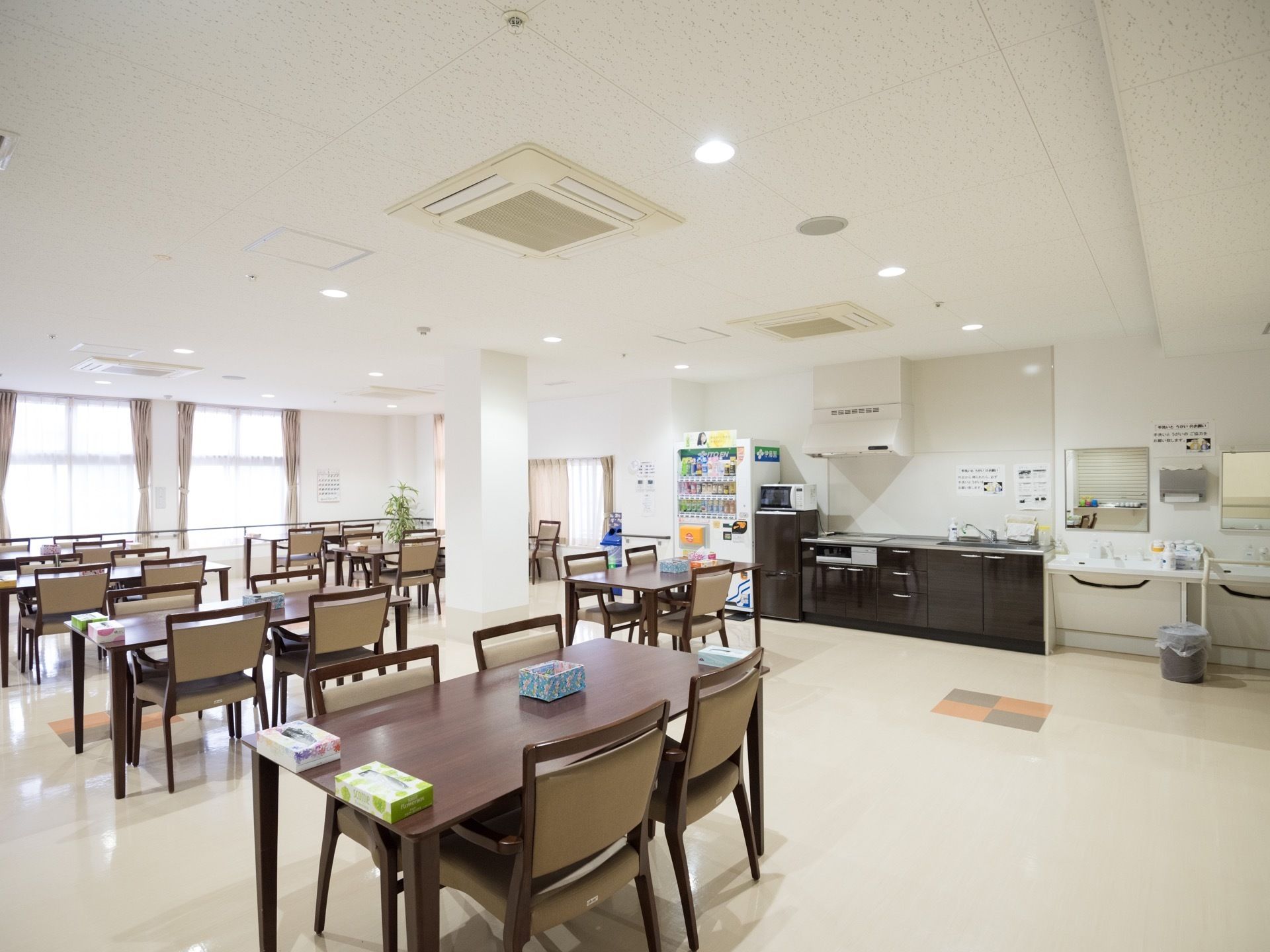 食堂は広く、複数のテーブルと椅子が並べられている。洗面台やキッチンスペースの横には自動販売機が設置されている。