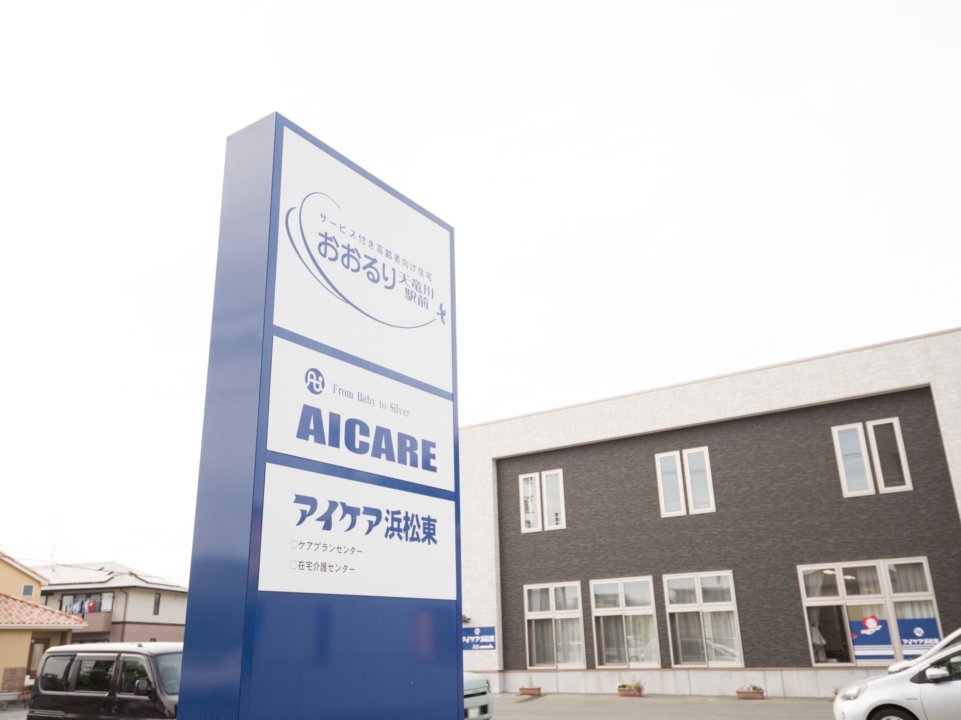施設は白色の縁にダークブランの配色がされている建物である。窓がいくつかあり、それぞれにカーテンがかけられている。青い看板が設置されている。