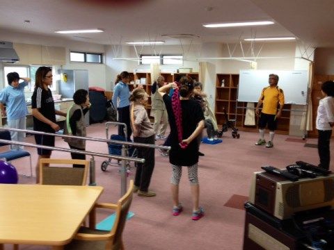 絨毯の広間でトレーナーと一緒にストレッチをする入居者様