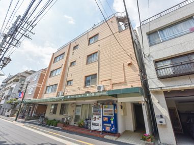 施設は4階建てで1階部分は建物から道路向きに緑色のひさしが取り付けられている。建物の前には自動販売機が2台設置されている。