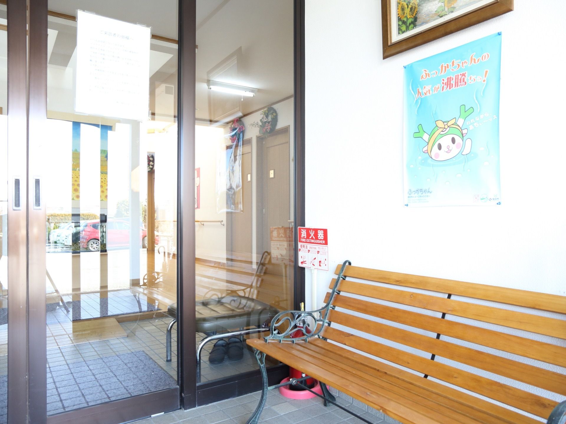 玄関は横開きの手動の扉となっている。ベンチと消火器が置かれている。壁にはポスターや絵画が飾られている。