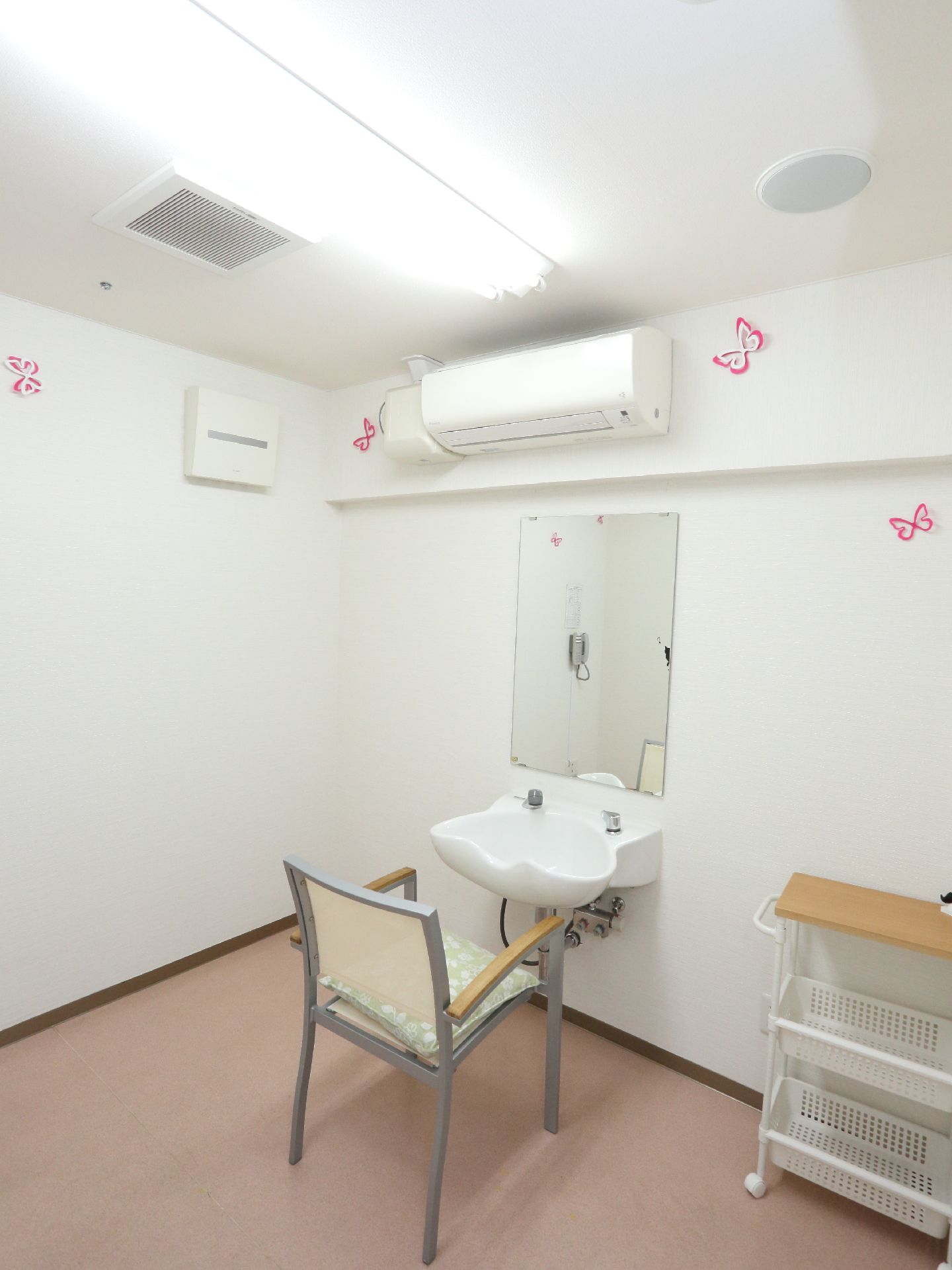 部屋の床は、薄ピンク色になっていて、洗髪台とパイプ椅子、コンセント、鏡、物置台がある。蝶々の飾りつけなどで、明るい雰囲気になっている。