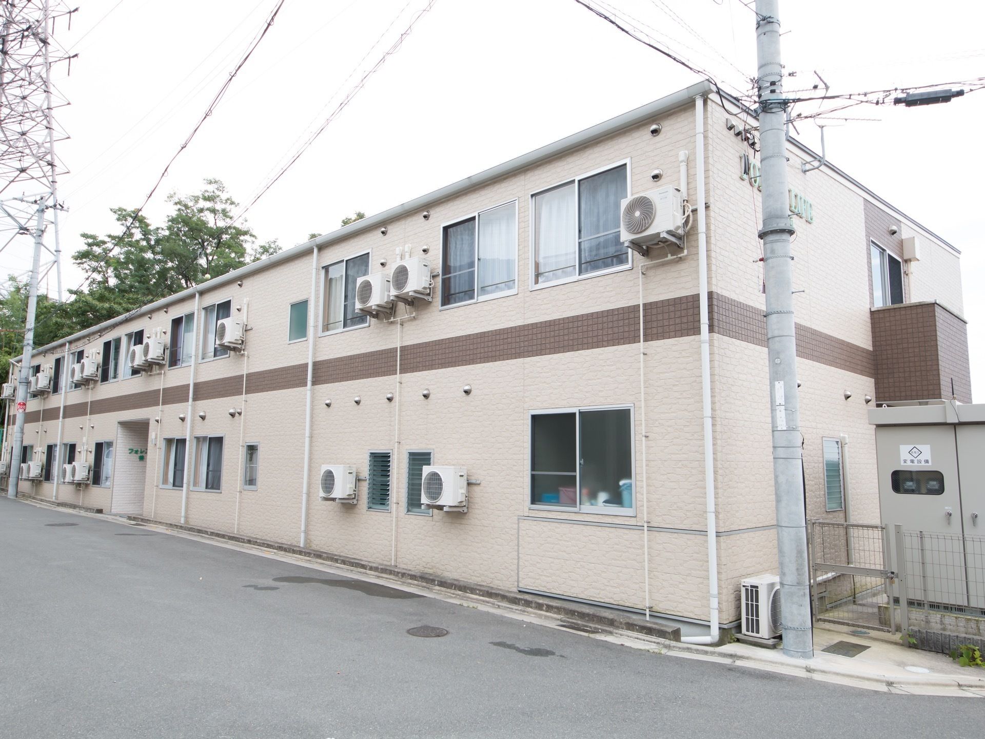 地上２階部分の様子で、ベージュを基本とした外壁となっている。空調設備の室外機は壁に取りつけられるタイプが使用されている。