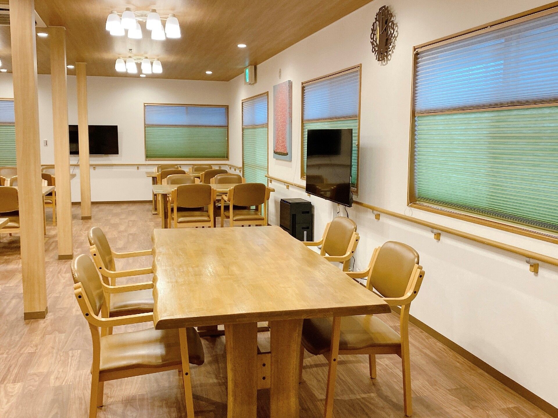複数の木製のテーブルにはそれぞれに椅子が配置されている。白い柱が数本立っている。テレビが設置されている。