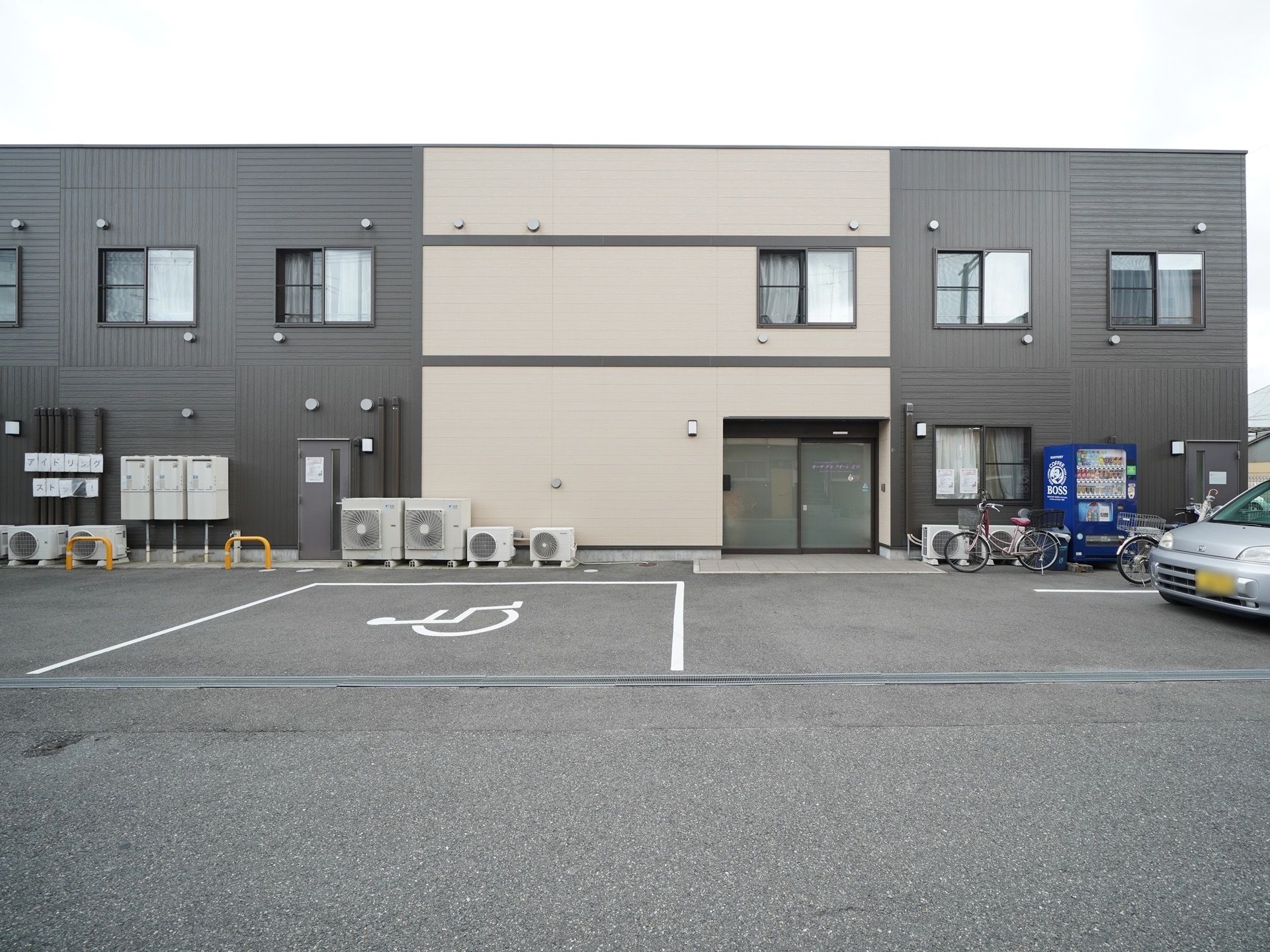 玄関付近に自動販売機が設置されてある。近くに車と自転車が止められている。入り口近くに駐車できるスペースがあるので安心して外出できる。