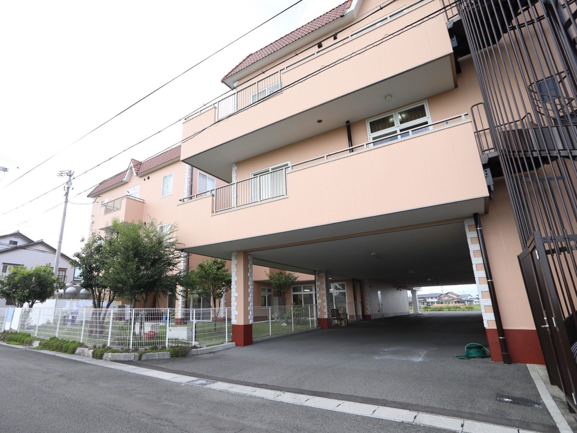 ３階建ての施設で、２階と３階にそれぞれベランダがある。建物の右側に黒い螺旋状の外階段がある。