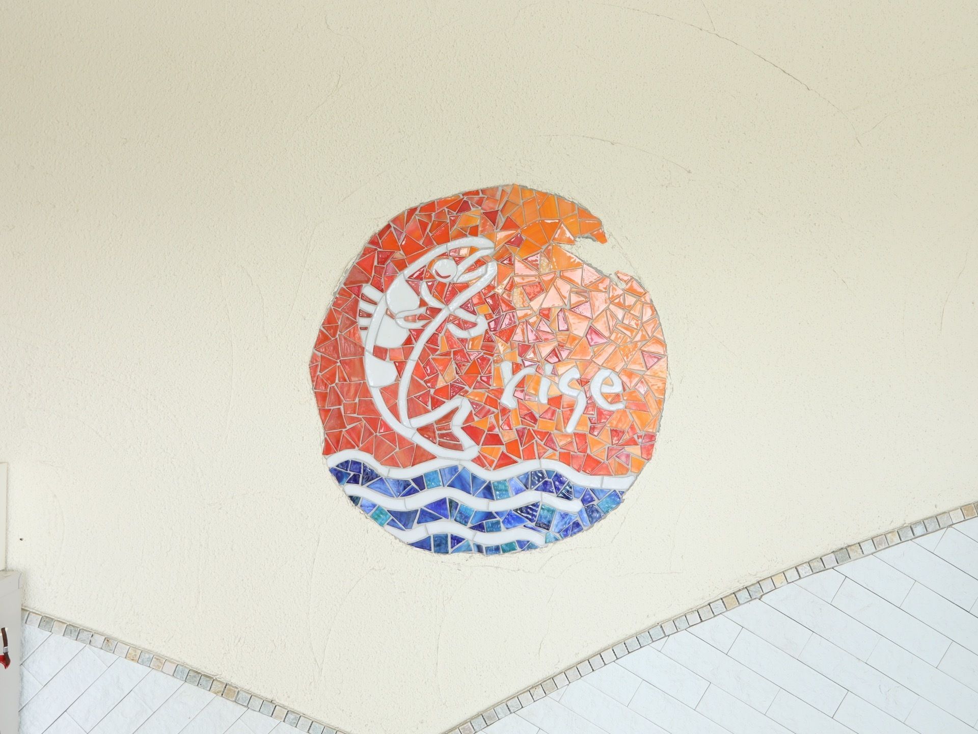 白い壁に、飛び跳ねる魚を描いたモザイクアートが施されている。白や水色、赤、オレンジなど鮮やかな色が使われている。