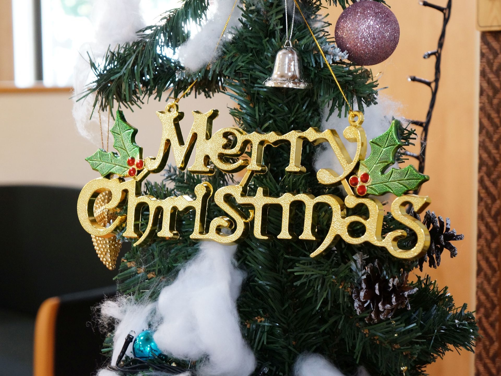 メリークリスマスと英語で書かれたオブジェがクリスマスツリーに飾られている。綿の雪やベル、キラキラの球体などの飾りもある。